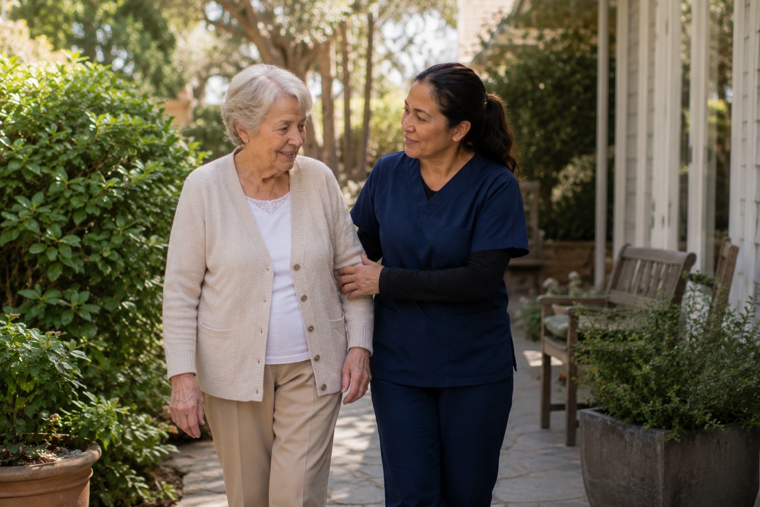 A caregiver walking arm in arm with an older woman along a garden path